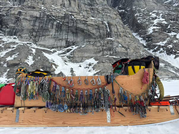 A wooden sled laden with rock climbing equipment, in front of a large rock wall
