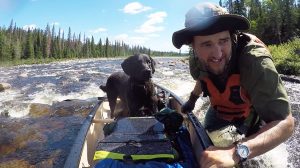 a man and a dog travel up a wild river in a canoe