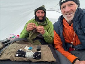 Two arctic travelers, Vincent Colliard and Borge Ousland, sit in their tent, making repairs while they wait out bad weather outside.