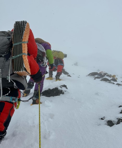 Climbers walking up on a snowy slope in foggy weather.