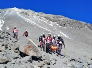Red Cross rescuers with mountaineering equipment carry a stretcher.