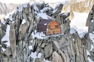 A cute little wodden cabin, surrounded by a metalic rail, perched by a col on a massive rocky face.