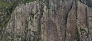 a small figure against a grey-brown cliff face
