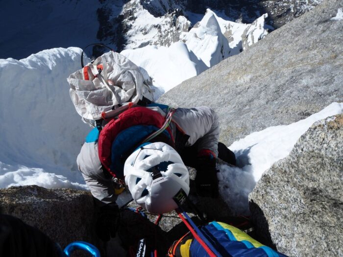 A climber on a vertical mixed pitch, as seen from above, shows a dmaaged helmet. 