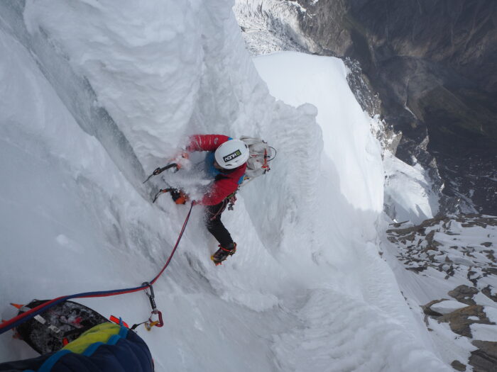 A climber as seen from above, hanging on vertical ice gullies with two ice axes and crampons.