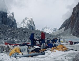 Climbers sitting on two chairs, surrunded by rags of tent and scattered items.