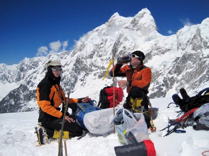 Climbers on a flat spot drinking water, ragged peaks under the sun in background. 