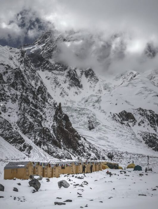 K2 and the Base Camp below dusted in fresh snow. Clouds wrap the mountain. 