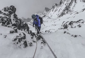 A climber descending down a mixed ramp in cloudy weather.