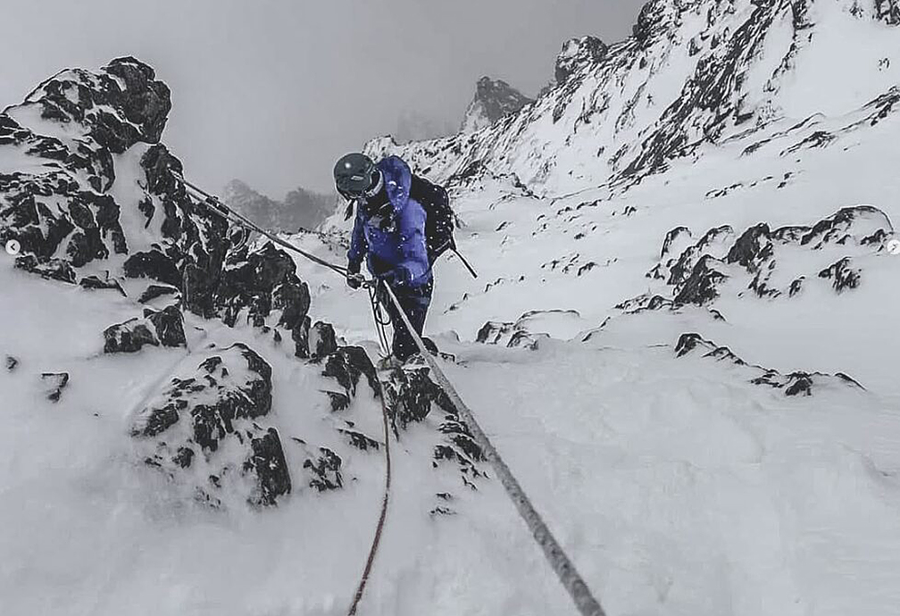 A climber descending down a mixed ramp in cloudy weather.