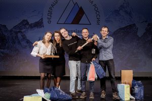 The winners stand on stage, smiling and holding their trophies.