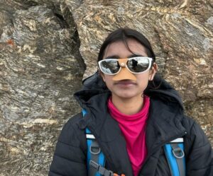 Selena in front of a rock wall, with sunglasses and nose protector.