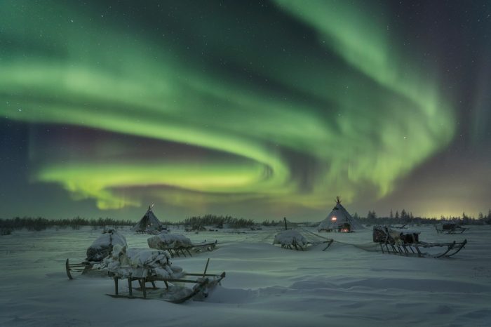A snowy campsite with the northern lights visible above.