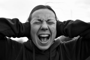 A woman screams with her hands over her ears.