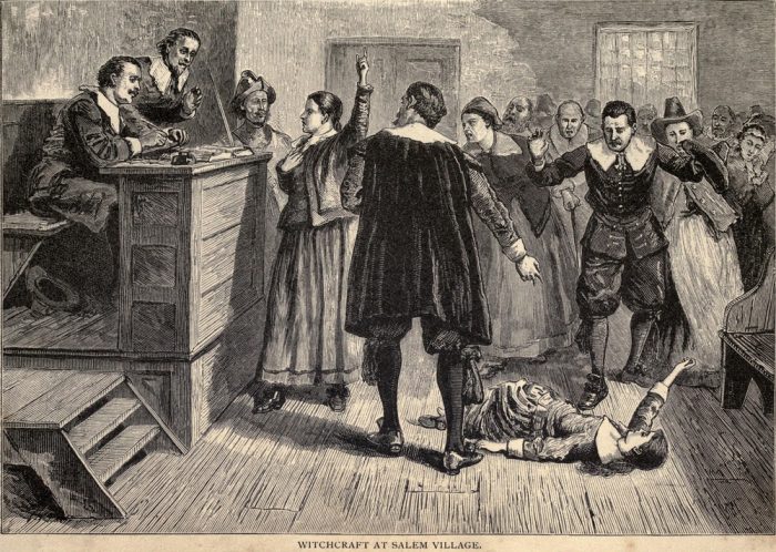 A group of people in a court house. A young woman lies on the ground while a crowd of people look on.