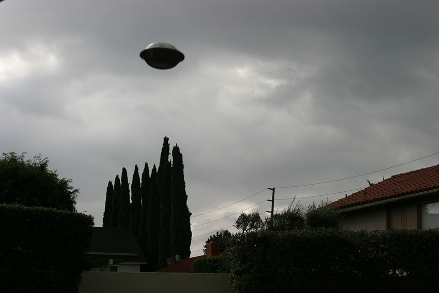 b/w illustration of flying saucer over some trees
