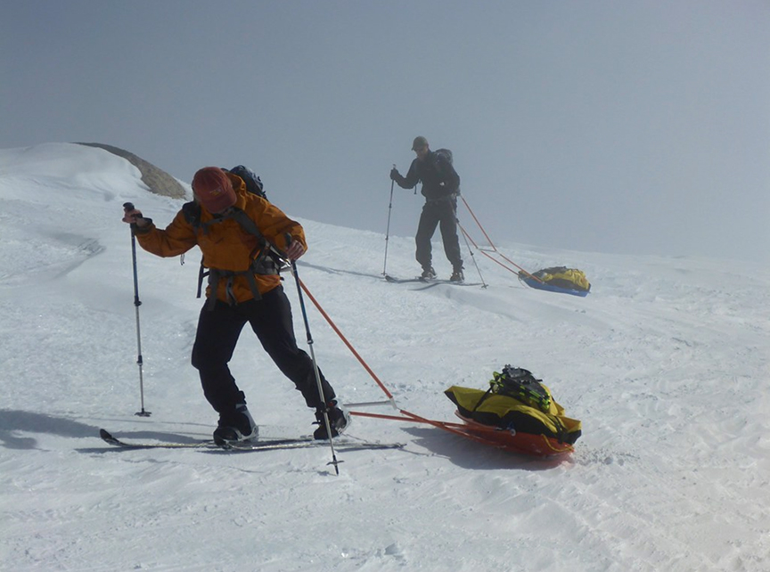 two skiers hauling sleds uphill in fog