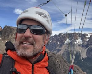 Close shot (selfie) of Carlos Suarez while he paraglides, with some mountains in background.