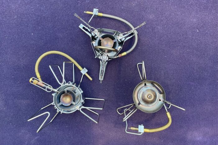 Three liquid-fuel stoves with a purple backdrop