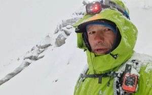 Video frame showing Kowalewski in a snowy day on a snow slope, a headlamp and hood on his gore-tex jacket.