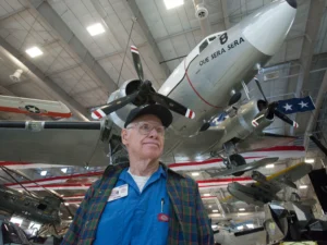 An elderly man, Conrad Shinn, stands proudly in front of a small plane