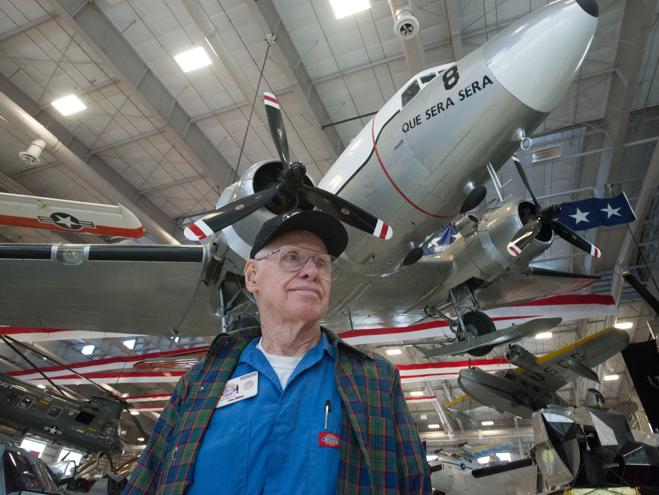 An elderly man, Conrad Shinn, stands proudly in front of a small plane